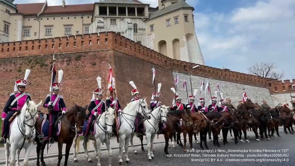 Ułani Krakowskiego Szwadronu Ułanów w paradnych mundurach, w szyku konno pod murami Wawelu. Kadr z filmu „Nowohucka Kronika Filmowa nr 721”, realizacja: Krzysztof Ridan, Ośrodek Kultury Norwida, licencja CC BY 4.0 (kadr przycięty).